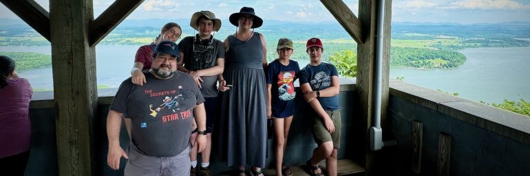 A family of father, mother, young woman, two young men, and a girl in front of an overlook above Lake Champlain in New York